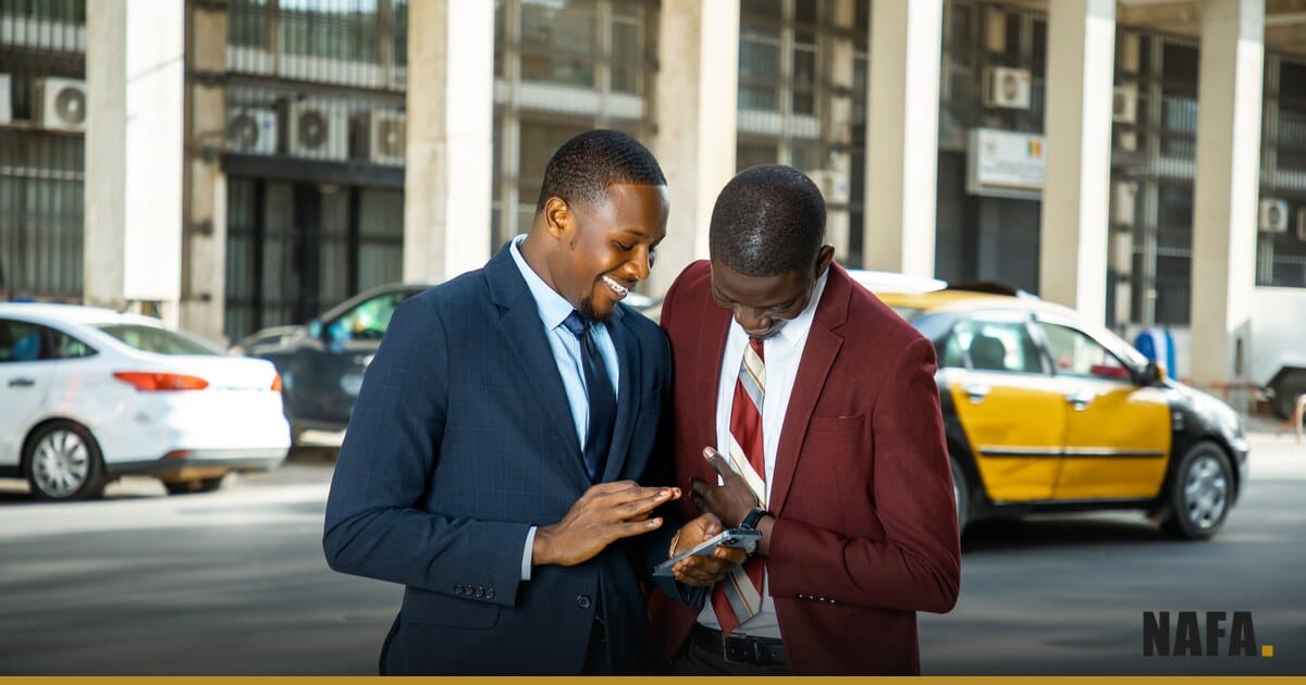 Deux hommes d'affaires en costume consultant un telephone dans une rue animee de Dakar