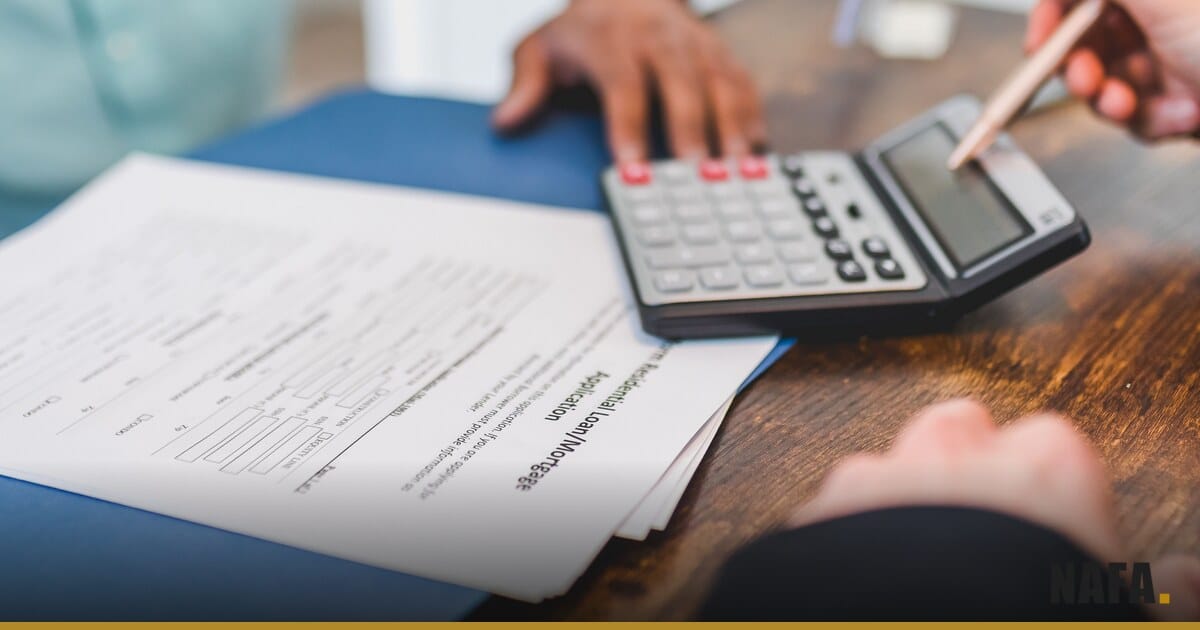 Mains signant un contrat de crédit à côté d'une calculatrice, illustration du coût d'un emprunt.