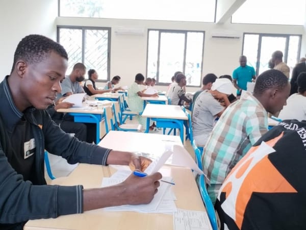 Candidats assis à des tables dans une salle d'examen, composant sur papier