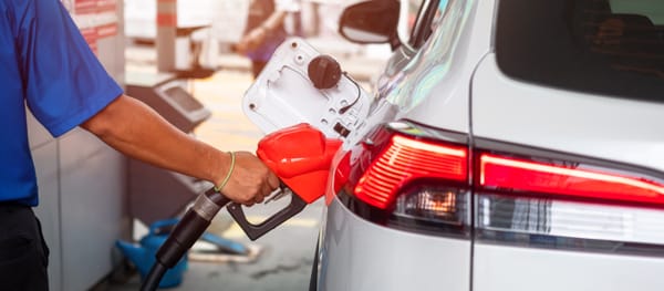 Pompiste tenant un pistolet de carburant rouge inséré dans le réservoir d'une voiture blanche